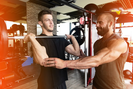 Personal Trainer Showing Young Man How to Train Shoulders With Barbell in the Gym
