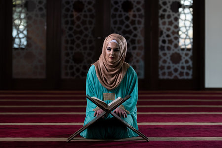 Muslim Woman Reading Koran or Quran Wearing Traditional Dress at the Mosque