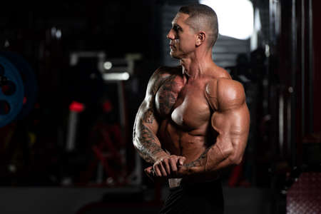 Handsome Man Standing Strong In The Gym And Flexing Muscles - Muscular Athletic Bodybuilder Fitness Model Posing After Exercisesの写真素材