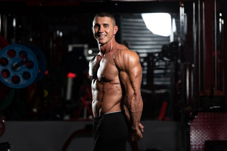 Handsome Man Standing Strong In The Gym And Flexing Muscles - Muscular Athletic Bodybuilder Fitness...