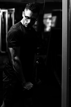 Fitness Man With Glasses Doing Heavy Weight Exercise For Triceps On Machine With Cable In The Gym