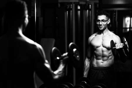 Athlete With Gynecomastia Breasts Problem Working Out Biceps In A Gym - Dumbbells Concentration Curlsの写真素材