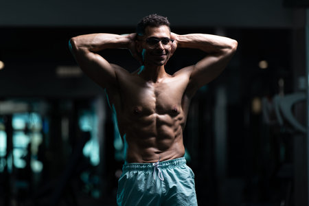 Young Man With Gynecomastia Breasts Problem Standing Strong In The Gym And Flexing Muscles