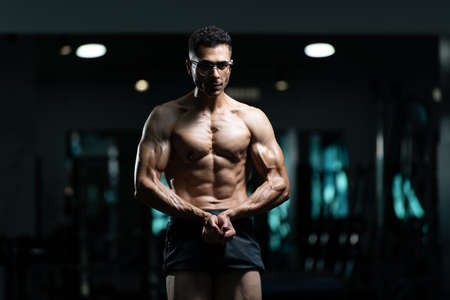 Handsome Young Man With Gynecomastia Breasts Problem Standing Strong In The Gym And Flexing Musclesの写真素材