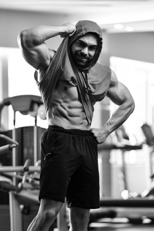 Healthy Young Man Standing Strong in the Gym and Flexing Muscles in a Hoodie - Muscular Athletic Bodybuilder Fitness Model Posing After Exercisesの写真素材