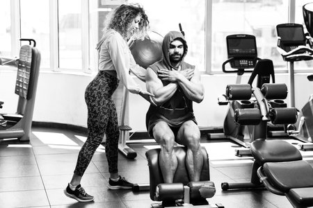 Young Adult Man Working Out in Gym - Doing Legs Exercise With Help of Her Personal Trainer