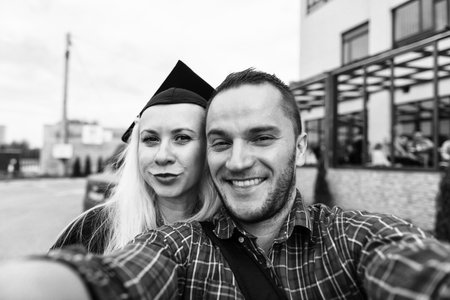 Portrait of Romantic Couple in Love Looking at Camera Making Selfie Woman Confidently Wearing Black Cap and Gown at Graduationの写真素材