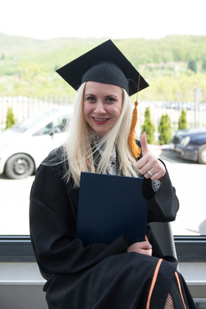 Young Happy Woman University Graduates in Graduation Gown and Cap Holds a Degree Certificate to Celebrate Her Education Achievement on the Commencement Dayの写真素材