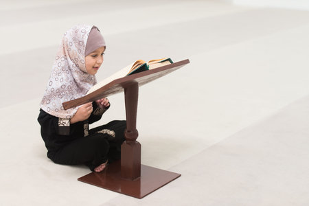 Portrait of a Muslim Young Girl Reading Holy Islamic Book Koran While Wearing A Traditional...