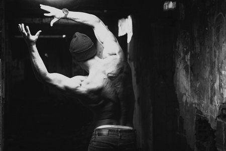 Handsome Young Man With Winter Hat Standing Strong Outdoors and Flexing Back Muscles in Ruins -...
