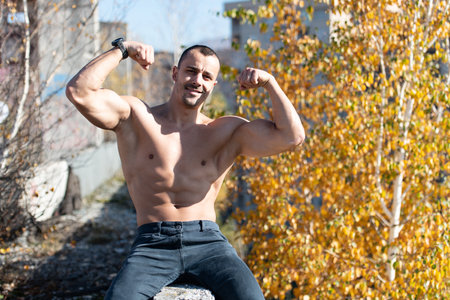 Healthy Young Man Sitting Strong Flexing Muscles on Old Rooftop - Muscular Athletic Bodybuilder Fitness Model Posing Outdoorsの写真素材