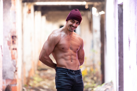 Handsome Young Man Standing Strong Outdoors and Flexing Muscles in Ruins - Muscular Athletic...