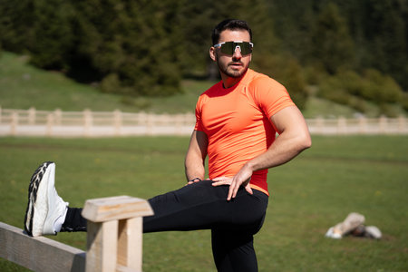 Young Man Stretching His Legs Using A Wooden Fence On A Beautiful Sunny Day In Natureの写真素材