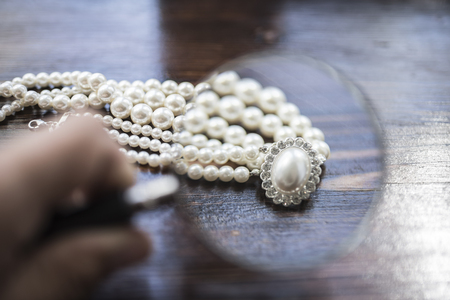 A necklace of white pearls with a large pearl surrounded by diamonds lies on a dark brown wooden backgroundの写真素材