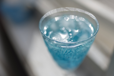 Alcohol cocktail of blue color with ice cubes in a transparent carved glass on a light backgroundの写真素材