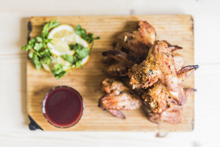 Chicken wings of a barbecue, red sauce, green parsley and lemon slices lie on a light bamboo cutting boardの写真素材