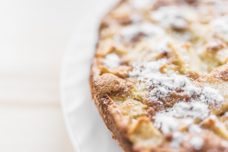 A fresh baked apple pie sprinkled with sugar powder lies on a white plate in the right side of the frame.の写真素材