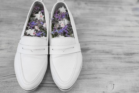 Female white shoes and small white and purple flowers inside on a white wooden backgroundの写真素材