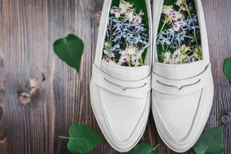 Women's white shoes with white and blue flowers inside for flavoring and green leaves next to a dark wooden backgroundの写真素材