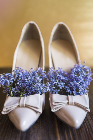 Women's beige lacquered high-heeled shoes with a sharp nose and bow and bright lilac flowers inside like a natural deodorant for shoes on a dark wooden and gold background.の写真素材
