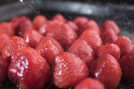 Bright red strawberry under the spray of drops of water on a black background, closeupの写真素材