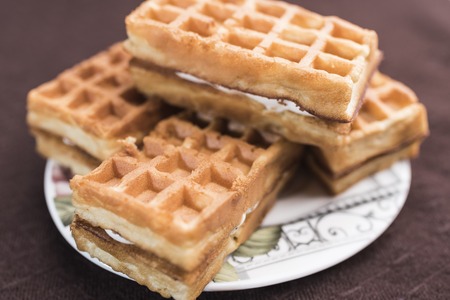 Delicious Viennese waffles with a filling lie on a saucer on a dark brown background, close-upの写真素材