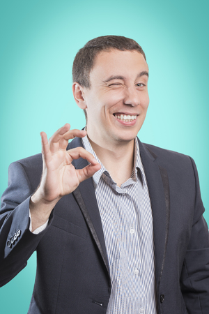 Businessman smiling, winking and showing gesture OK, isolated on green backgroundの写真素材