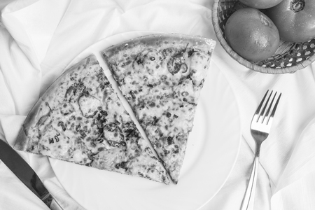 Two pieces of pizza on a white plate, fresh tomatoes, a fork and a knife, a black and white frameの写真素材