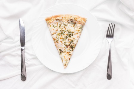 Piece of pizza on a plate, fork and knife on a white tableclothの写真素材