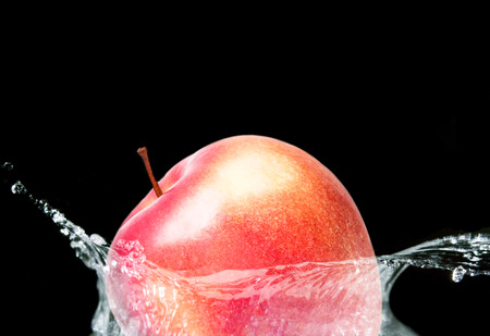 A red apple falling in water on blackの写真素材