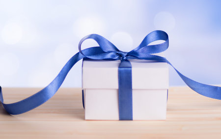 Christmas gift box with blue ribbon bow and bokeh background.