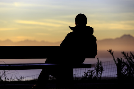 Silhouette of man on bench watching sunsetの写真素材