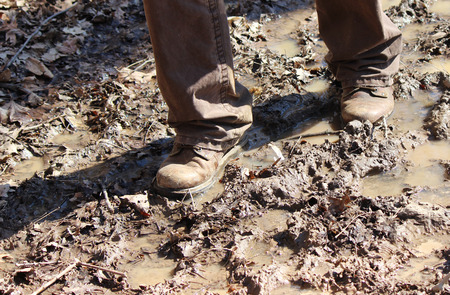 A man with boots walking on a muddy trail in Februaryの写真素材