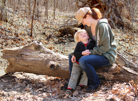 Blond boy and his mother smiling and enjoying a sunny day in late February sitting on a logの写真素材