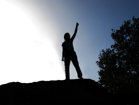Backlit of a person by lifting the arm as a sign of victoryの写真素材