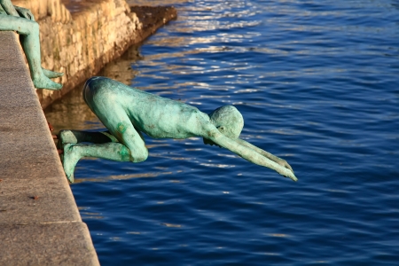 modern figures in bronze of child jumping into the sea from a pierの写真素材
