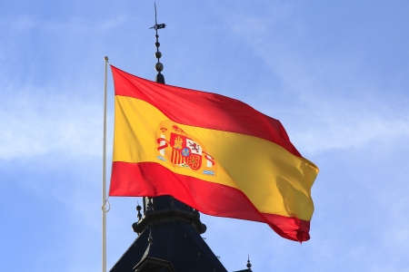 Spanish flag waving in the wind against a blue sky with cloudsの写真素材