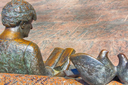 bronze statue woman sitting reading in a park benchの写真素材