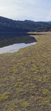 Calm lakeside view on a clear day with gentle ripples reflecting surrounding rocks and grassy shoreの写真素材