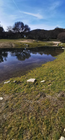 Calm lakeside view on a clear day with gentle ripples reflecting surrounding rocks and grassy shoreの写真素材
