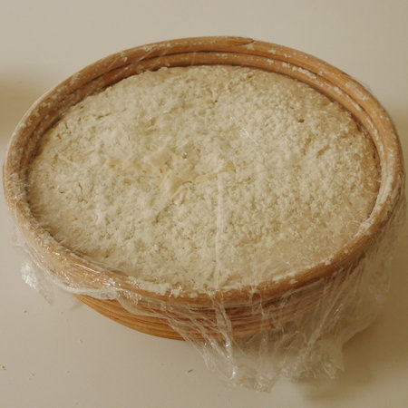 Sour bread dough proving in basket covered with cling film