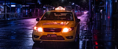 A Melbourne City yellow taxi cab on a rainy night with wet streets and light glowsの写真素材