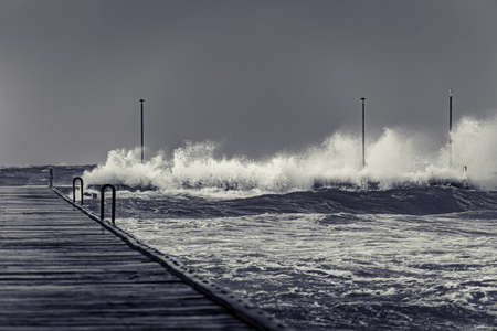 Waves swallowing end of Frankston pier on a gloomy stormy day in black and whiteの写真素材