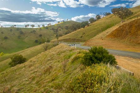 Winding Australian country road through a dry grassy hillside vistaの写真素材
