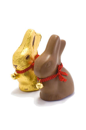 A golden and chocolate Easter bunny sit side by side on a white background の写真素材