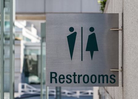 A modern public restrooms sign made from brushed metal attached to a concrete wall の写真素材