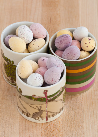 Three decorative egg cups full of mini chocolate Easter eggs on a pine table 