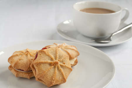 An afternoon tea table setting of white porcelain on a cotton tablecloth with Viennese whirls and a cup of teaの写真素材