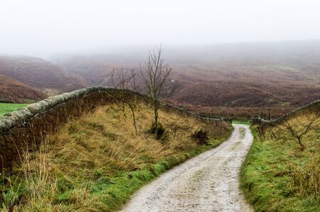 A farm track winds towards foggy moorsの写真素材
