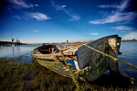 Abandoned boat under blue sky moored up in the weeds on a riverのeditorial素材